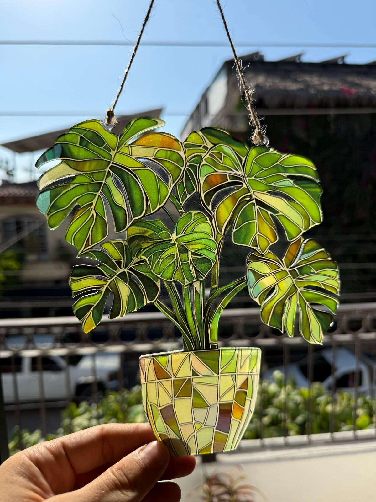 Stained glass plant decoration held by a hand with a blurred outdoor background